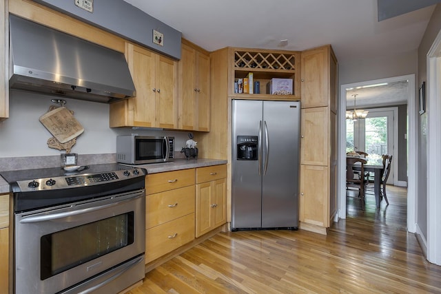 kitchen featuring light brown cabinetry, a chandelier, light wood-type flooring, stainless steel appliances, and wall chimney exhaust hood