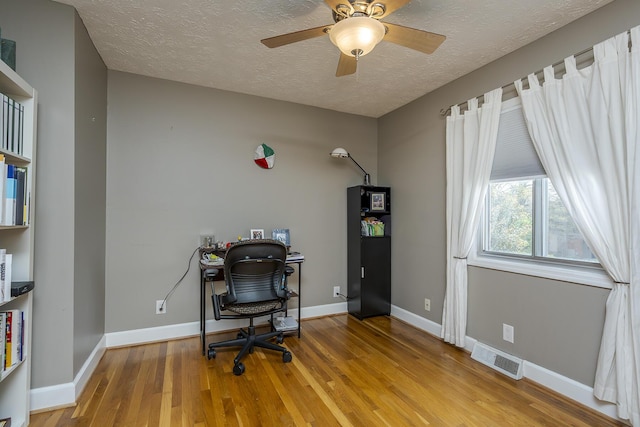 office featuring wood finished floors, visible vents, baseboards, a textured ceiling, and ceiling fan