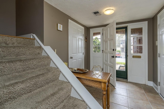 entryway featuring visible vents, light tile patterned floors, baseboards, a textured ceiling, and stairs