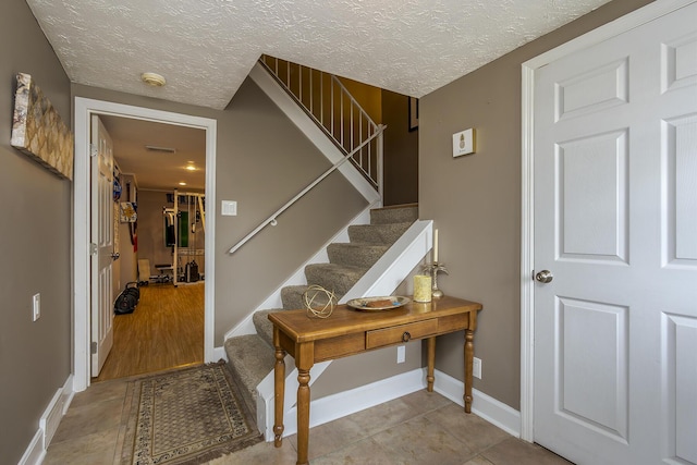 foyer entrance featuring stairway, a textured ceiling, and baseboards