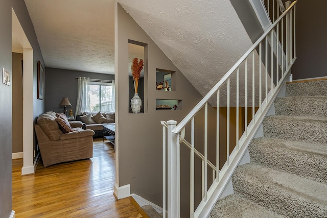 stairs with wood finished floors, a textured ceiling, lofted ceiling, and baseboards