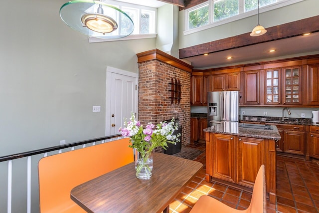 kitchen with a center island, a towering ceiling, glass insert cabinets, brown cabinets, and stainless steel fridge with ice dispenser