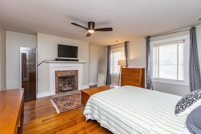 bedroom featuring wood finished floors, a brick fireplace, a ceiling fan, and baseboards