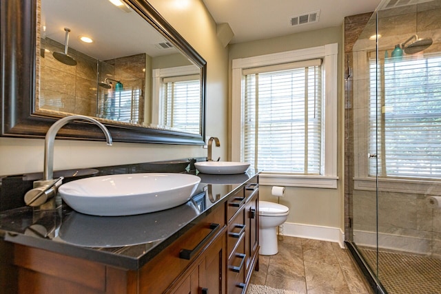 bathroom featuring a shower stall, a sink, double vanity, baseboards, and visible vents