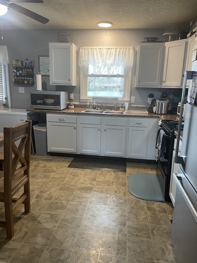 kitchen with a ceiling fan, a sink, stainless steel microwave, black range with electric cooktop, and a textured ceiling