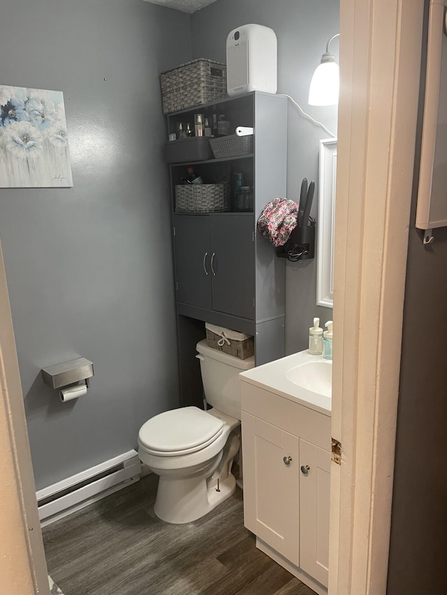 half bathroom featuring a baseboard heating unit, wood finished floors, vanity, and toilet