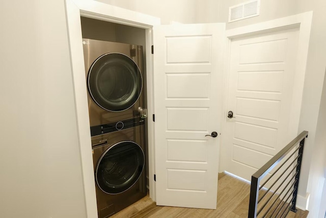 laundry area featuring laundry area, visible vents, stacked washer and clothes dryer, and light wood-type flooring