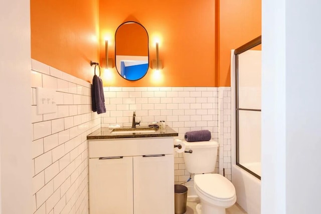 bathroom with tile walls, a wainscoted wall, vanity, combined bath / shower with glass door, and toilet