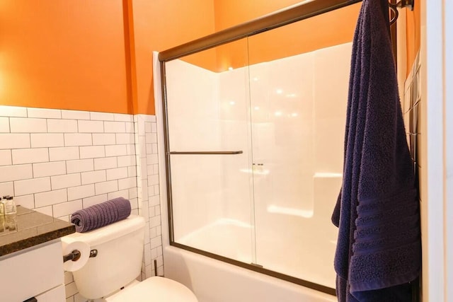 full bath featuring tile walls, bath / shower combo with glass door, vanity, and toilet