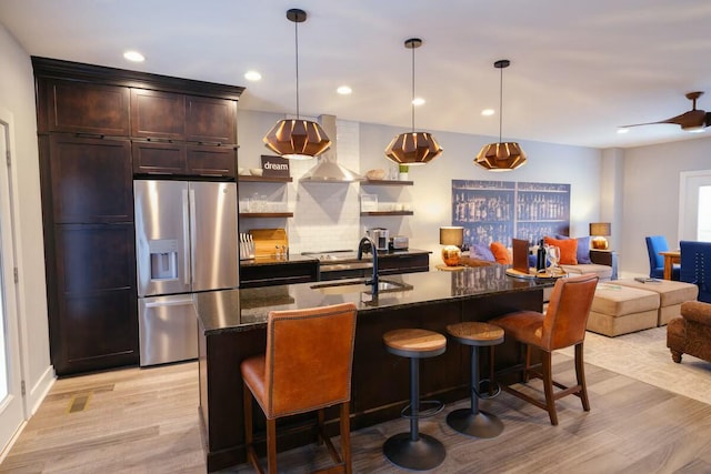 kitchen with a kitchen bar, stainless steel refrigerator with ice dispenser, a sink, dark stone countertops, and light wood-style flooring