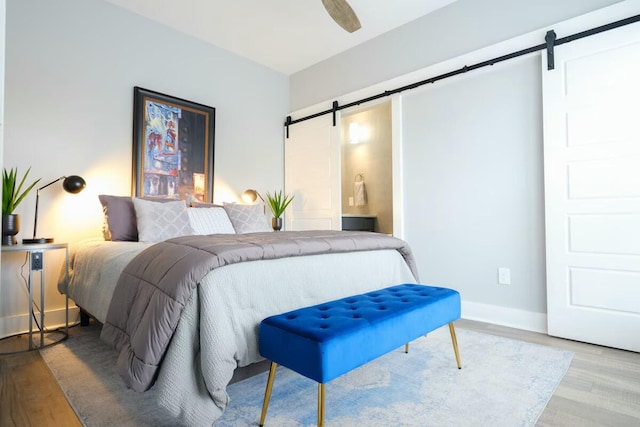 bedroom featuring baseboards, a barn door, wood finished floors, and ensuite bath