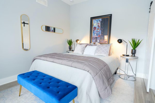 bedroom with visible vents, a barn door, baseboards, and wood finished floors