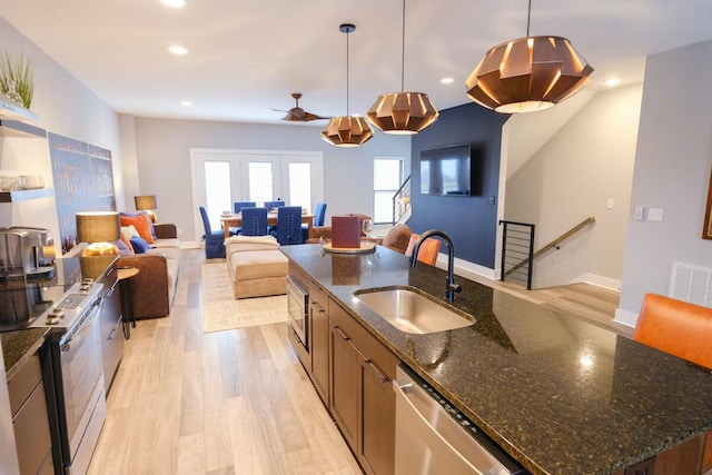 kitchen featuring appliances with stainless steel finishes, a sink, light wood-style floors, an island with sink, and recessed lighting