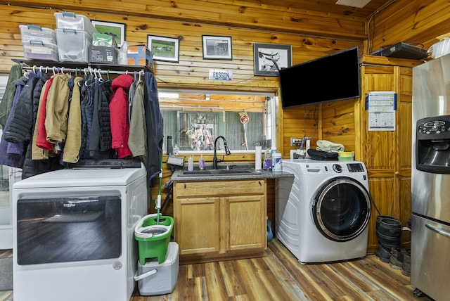 laundry room with light wood-type flooring, a sink, washer / clothes dryer, and wooden walls