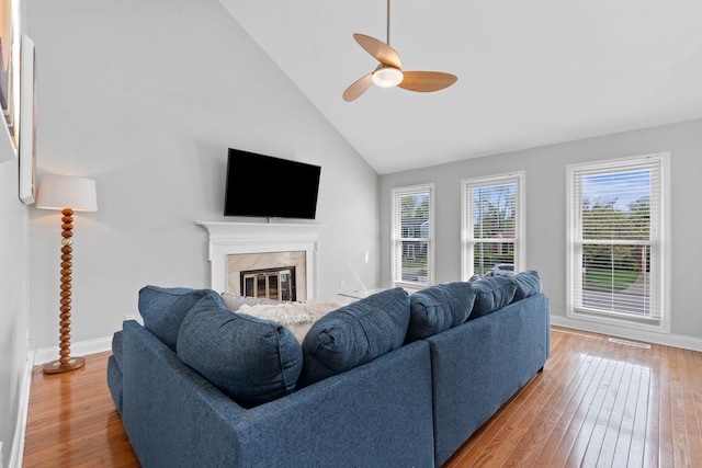 living area featuring light wood finished floors, high vaulted ceiling, a glass covered fireplace, a ceiling fan, and baseboards