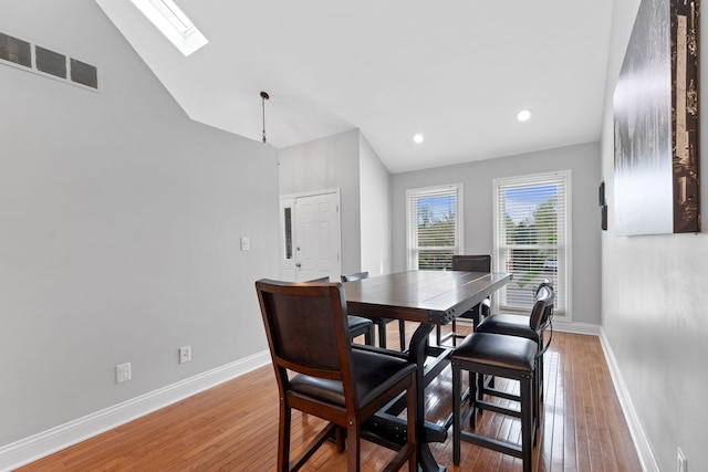 dining space featuring visible vents, light wood finished floors, baseboards, and vaulted ceiling with skylight