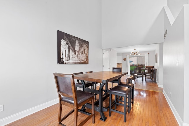 dining area with a high ceiling, an inviting chandelier, baseboards, and light wood finished floors