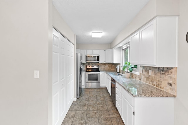kitchen with white cabinets, tasteful backsplash, light stone counters, a sink, and stainless steel appliances