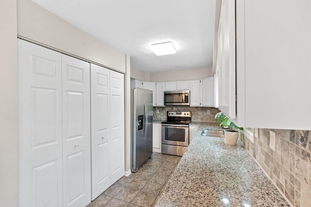 kitchen with decorative backsplash, a sink, light stone counters, stainless steel appliances, and white cabinetry