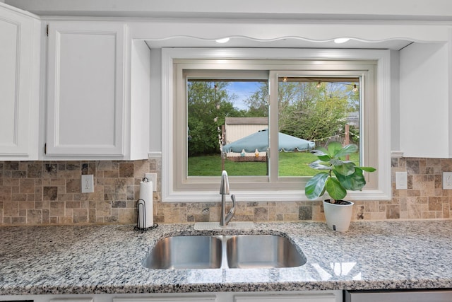interior details featuring dishwasher, white cabinets, light stone counters, a sink, and backsplash