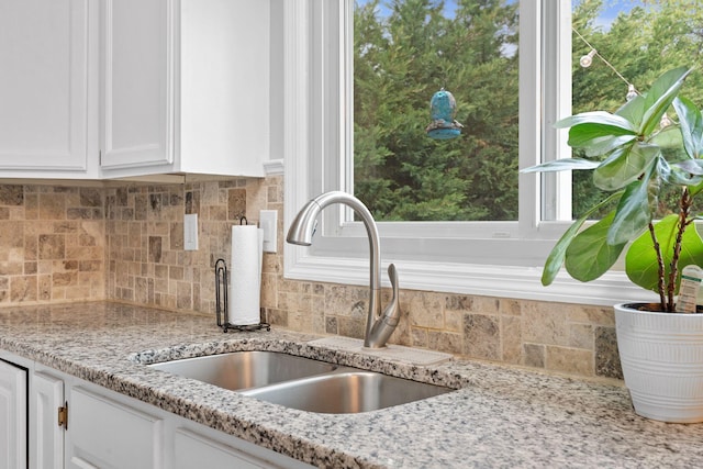 interior details with a sink, decorative backsplash, white cabinets, and light stone counters