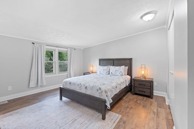 bedroom with a textured ceiling, visible vents, wood finished floors, baseboards, and ornamental molding