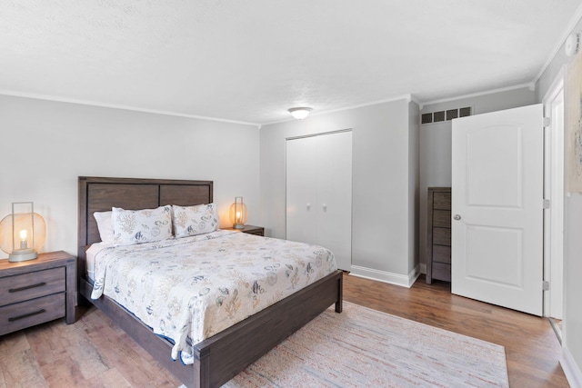 bedroom with visible vents, crown molding, wood finished floors, baseboards, and a closet