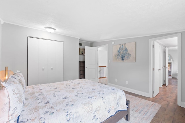 bedroom with a textured ceiling, baseboards, wood finished floors, ornamental molding, and a closet