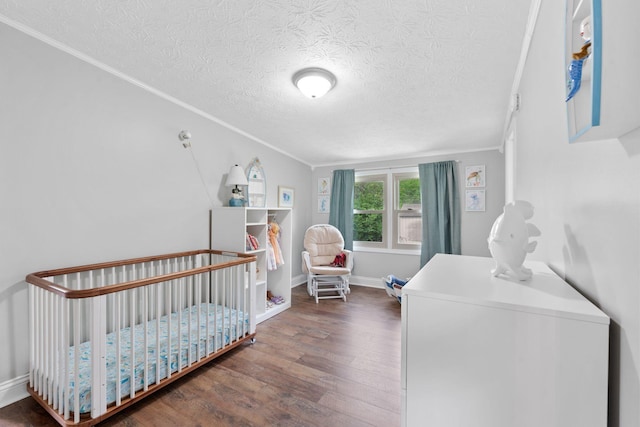 bedroom with crown molding, a nursery area, a textured ceiling, baseboards, and wood finished floors