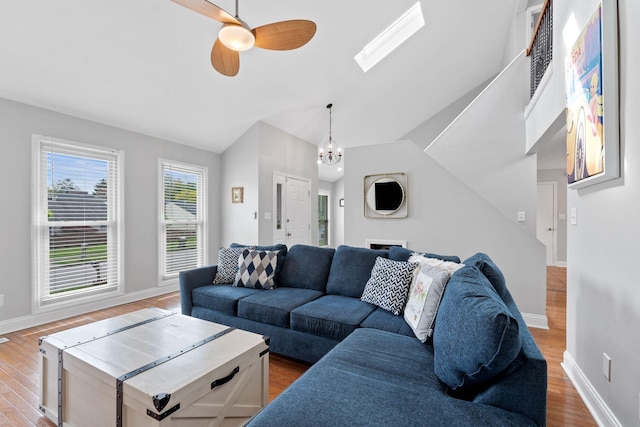 living room with vaulted ceiling with skylight, baseboards, ceiling fan with notable chandelier, and wood finished floors