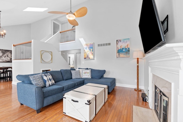 living room with visible vents, a fireplace, ceiling fan with notable chandelier, a high ceiling, and light wood-style flooring