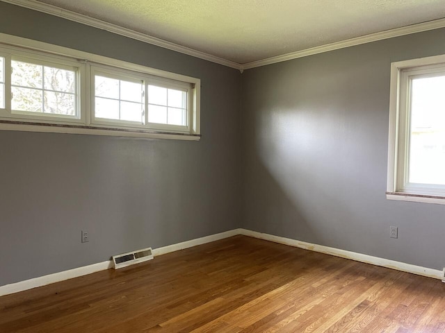 unfurnished room featuring wood finished floors, visible vents, a wealth of natural light, and crown molding