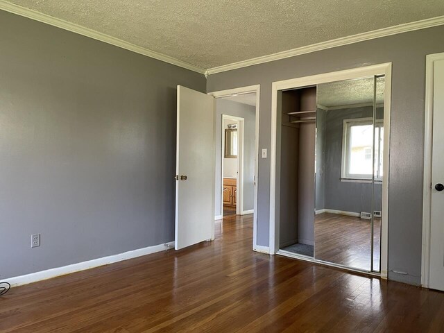 unfurnished bedroom featuring a textured ceiling, baseboards, wood finished floors, a closet, and ornamental molding
