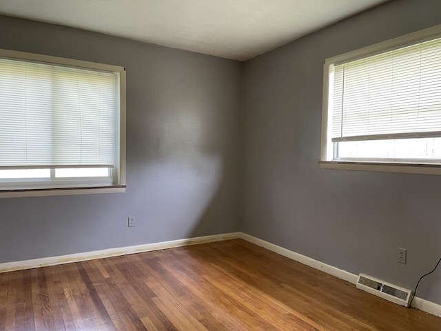 empty room featuring wood finished floors, visible vents, and baseboards
