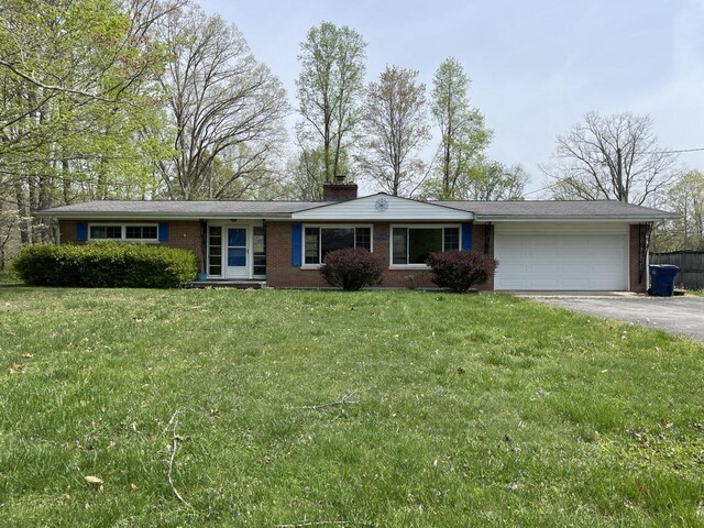ranch-style house with a chimney, a front lawn, an attached garage, driveway, and brick siding