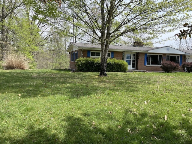 view of front facade with a chimney, brick siding, and a front yard