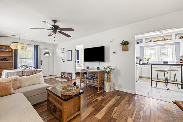 living area with light wood-style flooring, a ceiling fan, and baseboards