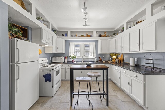 kitchen featuring dark countertops, white appliances, a sink, and white cabinetry