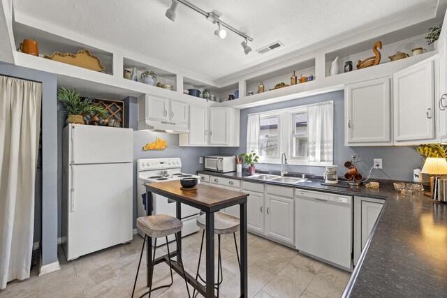 kitchen with white cabinets, a sink, dark countertops, white appliances, and under cabinet range hood