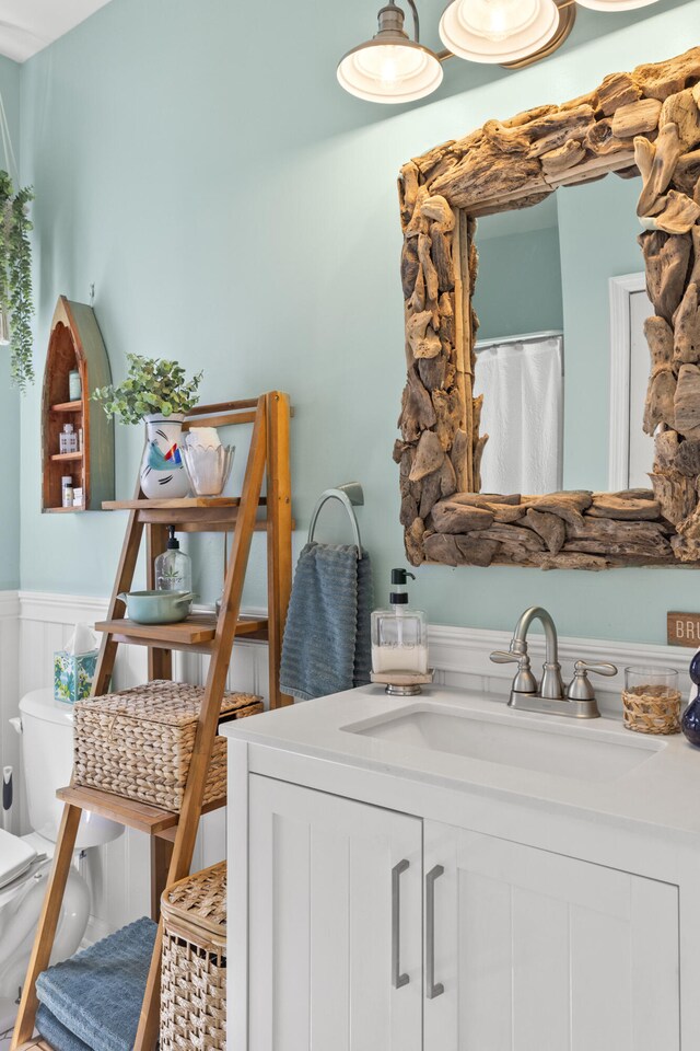 bathroom featuring toilet, vanity, and a wainscoted wall