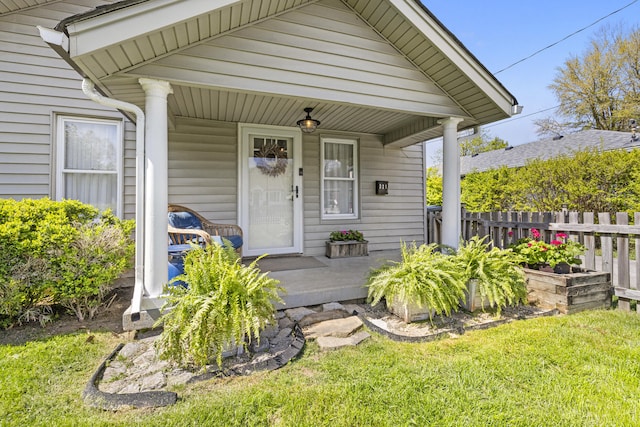 view of exterior entry with fence, a lawn, and covered porch