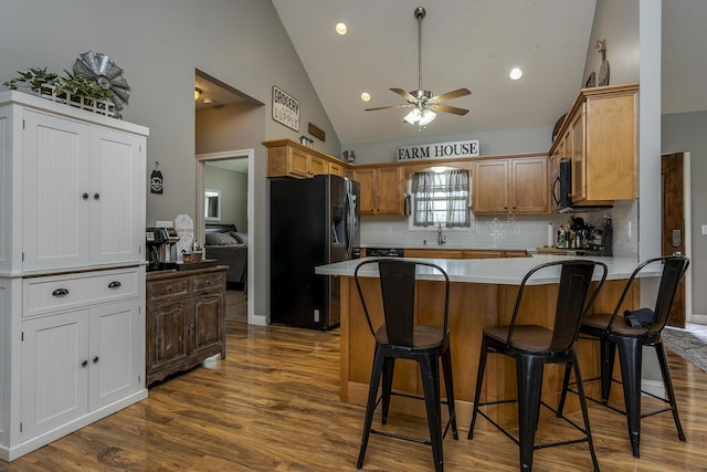 kitchen with a breakfast bar, dark wood-style flooring, a ceiling fan, a peninsula, and refrigerator with ice dispenser