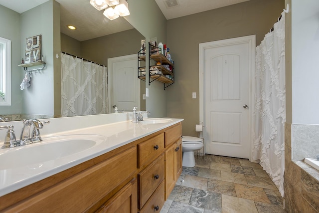 bathroom with toilet, double vanity, a sink, and stone finish floor