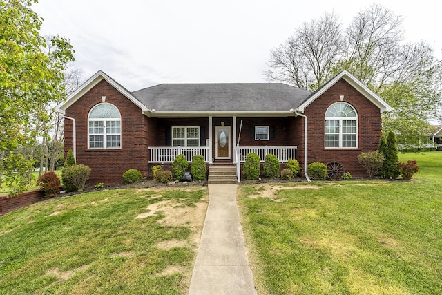 single story home featuring a front yard, a shingled roof, covered porch, and brick siding