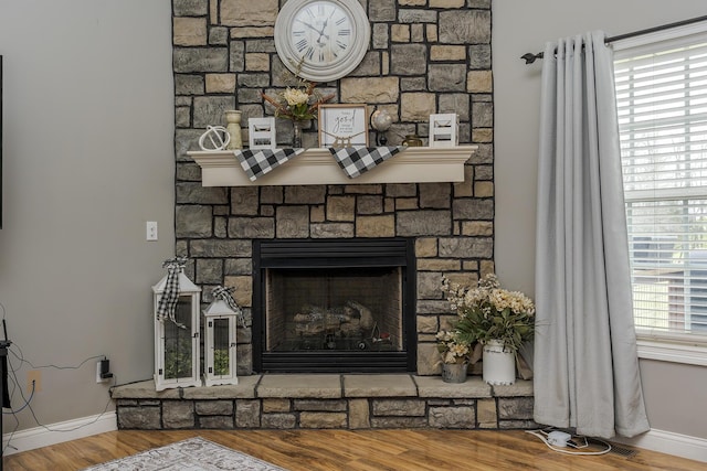 details with baseboards, wood finished floors, and a stone fireplace
