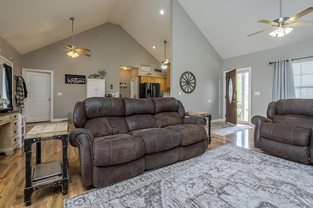 living room featuring ceiling fan, light wood-type flooring, high vaulted ceiling, and baseboards