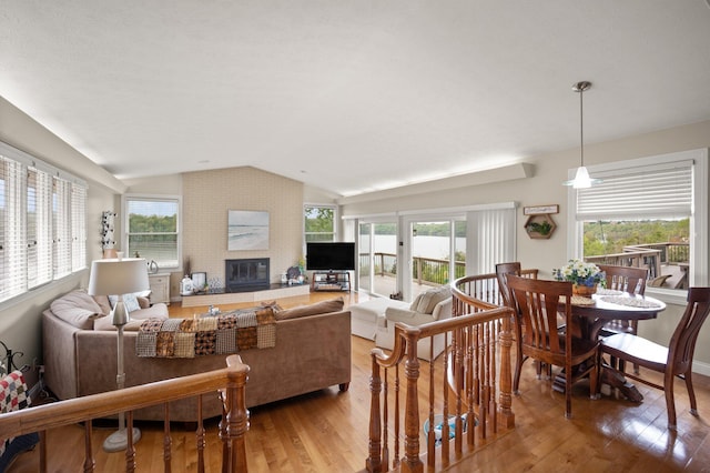 living room with a brick fireplace, a wealth of natural light, wood finished floors, and lofted ceiling