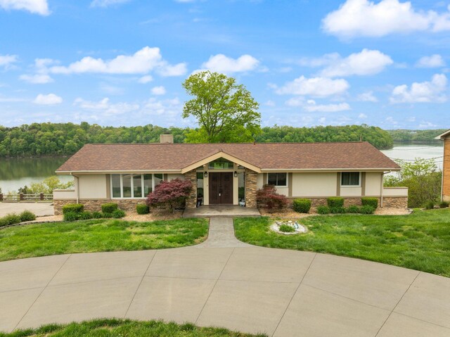 ranch-style house with a water view, a chimney, stucco siding, and stone siding