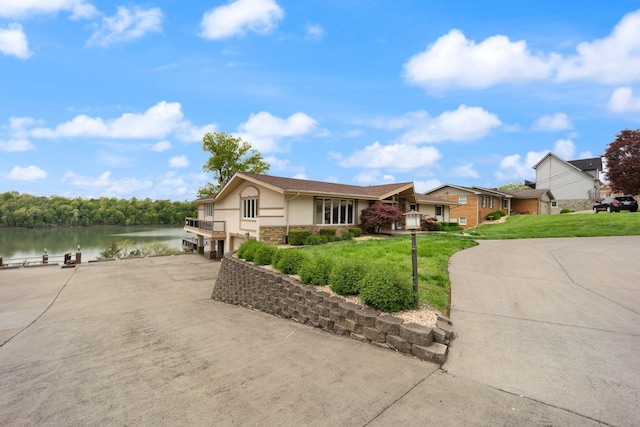 single story home featuring a front yard, stucco siding, concrete driveway, an attached garage, and a water view