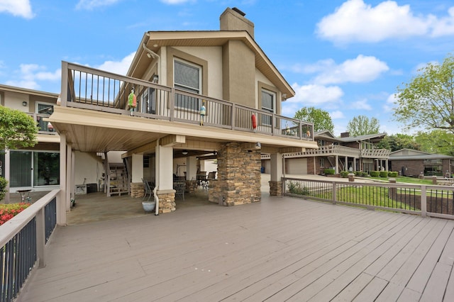 back of house featuring a deck, a chimney, a balcony, and stucco siding
